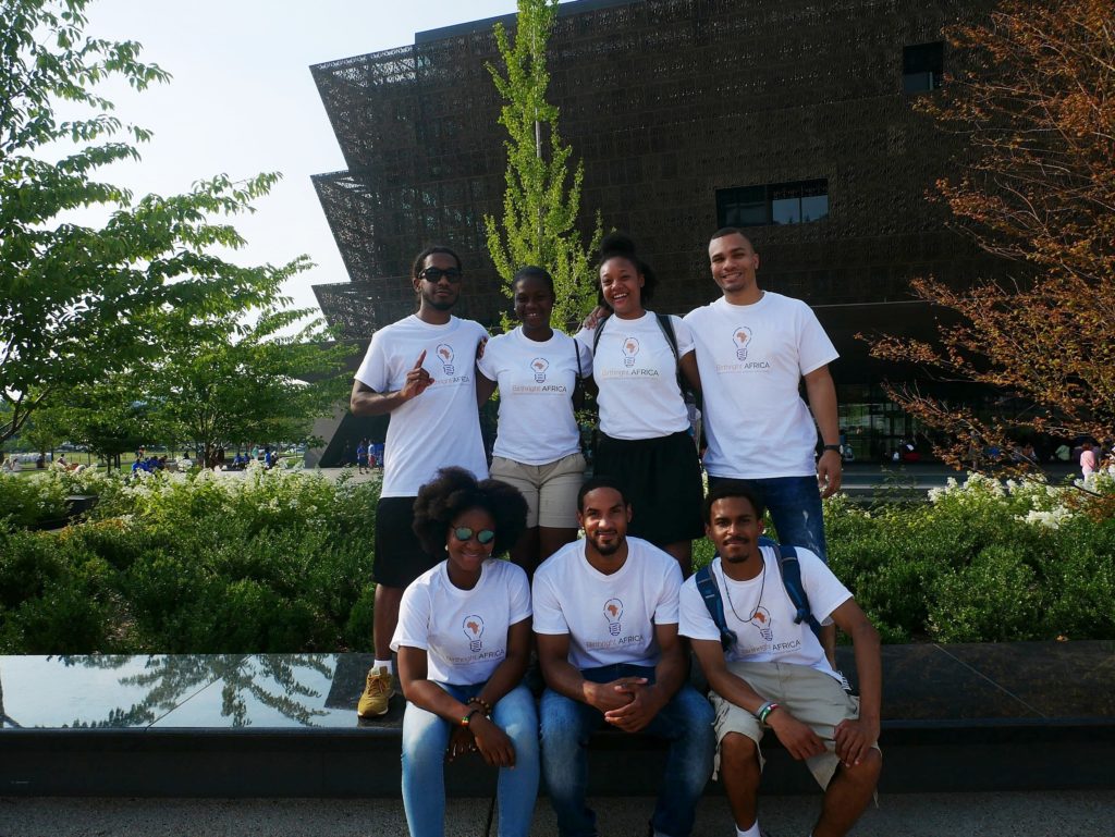 Seven students in Birthright Africa t-shirts stand in front of the Smithsonian National Museum of African American History and Culture